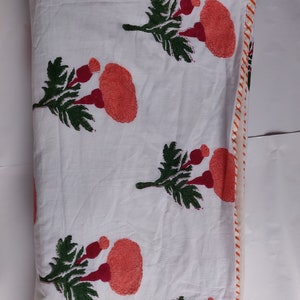 May include: White cotton quilt with a red and green floral print. The quilt has a white and orange striped border.