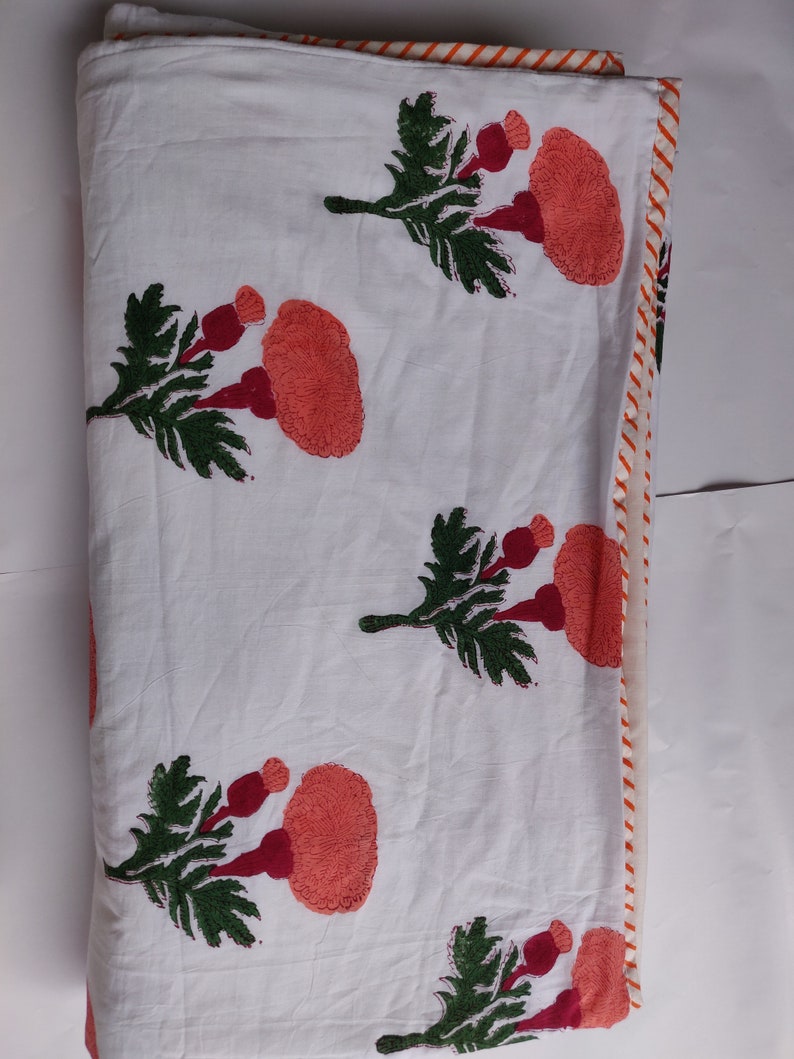 May include: White cotton quilt with a red and green floral print. The quilt has a white and orange striped border.