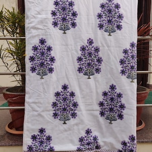 May include: White cotton fabric with a repeating pattern of purple floral bouquets. The fabric has a white border with a thin purple stripe.