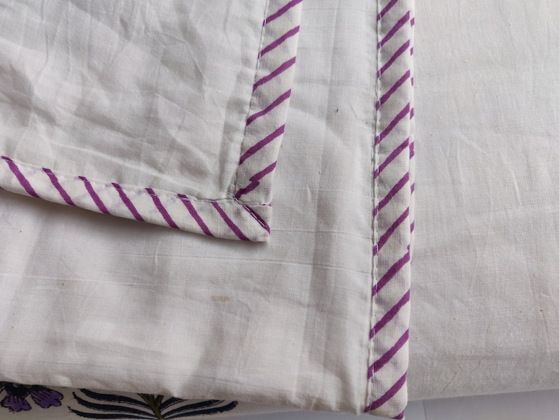 May include: White cotton fabric with a purple and white striped border. The fabric has a subtle texture.