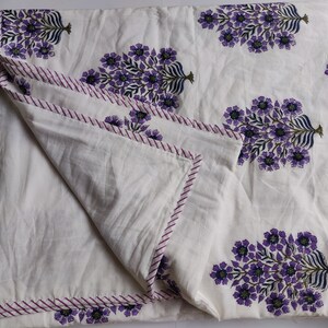 May include: White cotton quilt with a purple floral print. The quilt has a pink and white striped border.