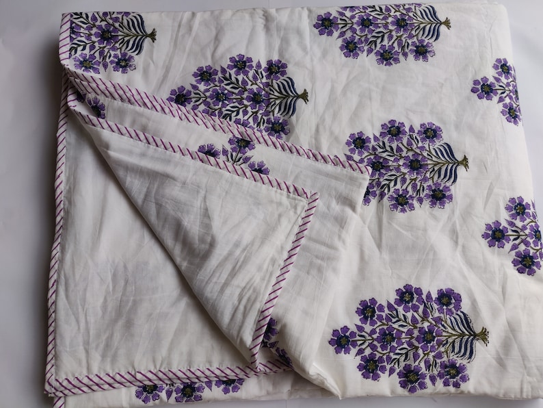 May include: White cotton quilt with a purple floral print. The quilt has a pink and white striped border.