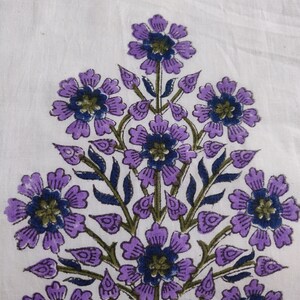 May include: A white fabric with a purple floral print. The flowers are arranged in a cluster and have a dark blue center.
