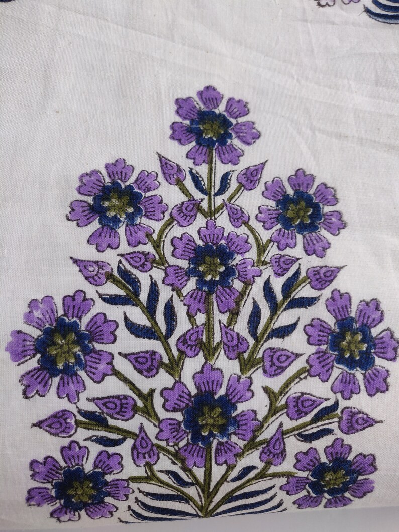 May include: A white fabric with a purple floral print. The flowers are arranged in a cluster and have a dark blue center.