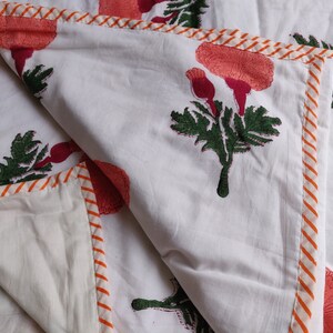 May include: White cotton quilt with a floral print in shades of pink, green, and orange. The quilt has a white and orange striped border.