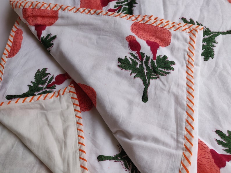 May include: White cotton quilt with a floral print in shades of pink, green, and orange. The quilt has a white and orange striped border.