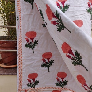 May include: White cotton quilt with a repeating pattern of orange flowers and green leaves. The quilt has a red and orange striped border.