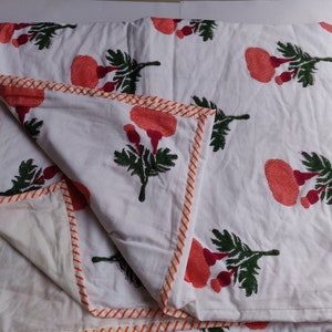 May include: White cotton quilt with a floral print of orange flowers and green leaves. The quilt has an orange and white striped border.