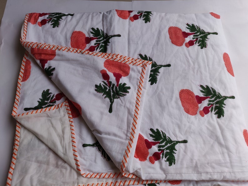 May include: White cotton quilt with a floral print of orange flowers and green leaves. The quilt has an orange and white striped border.