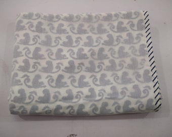 Könnte beinhalten: Eine weiße Babydecke aus Baumwolle mit einem blau-weiß gestreiften Rand. Die Decke hat ein sich wiederholendes Muster aus grauen, stilisierten Affen.