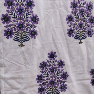 May include: White fabric with a repeating pattern of purple and blue floral designs. The flowers are stylized and resemble a tree branch with leaves and blossoms.