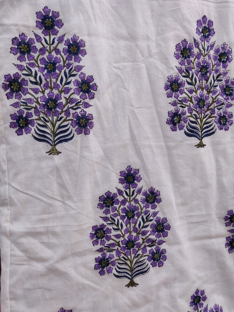 May include: White fabric with a repeating pattern of purple and blue floral designs. The flowers are stylized and resemble a tree branch with leaves and blossoms.