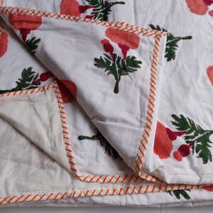 May include: White cotton quilt with a floral print of pink and green flowers. The quilt has an orange and white striped border.