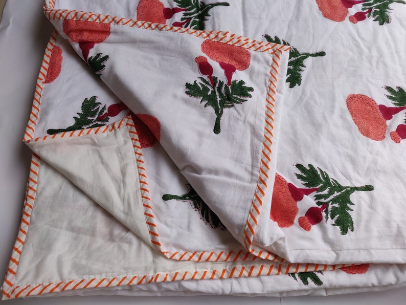 May include: White cotton quilt with a floral print of pink and green flowers. The quilt has an orange and white striped border.