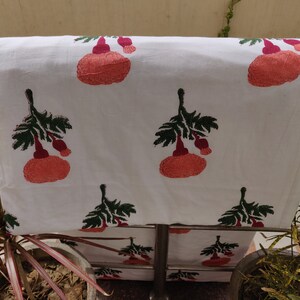 May include: White cotton fabric with a repeating pattern of pink and green floral designs. The fabric is folded and draped over a metal bar.
