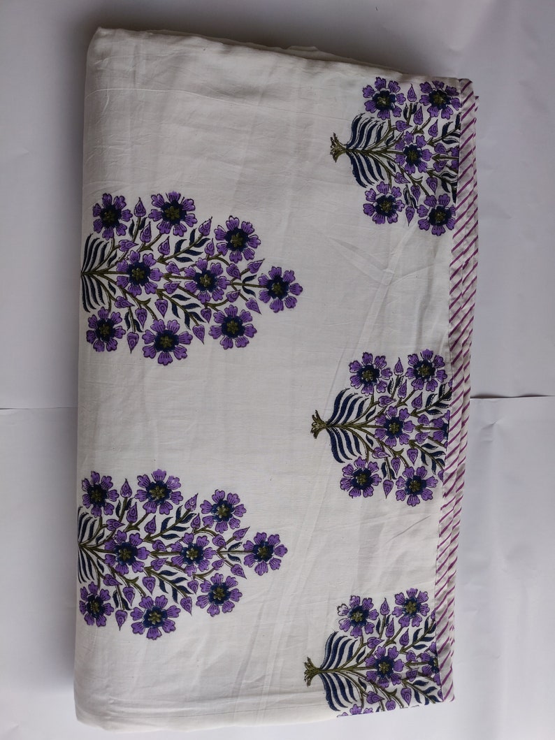 May include: White cotton fabric with a purple floral print. The fabric has a striped border in pink and white.