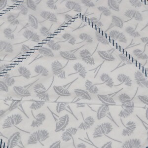 May include: White fabric with a repeating pattern of gray floral designs. The edges are trimmed with a navy blue stitched border. The fabric appears to be folded, creating a layered effect.