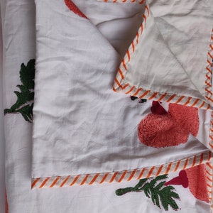 May include: White cotton quilt with a red and orange floral print. The quilt has a striped orange and white border.