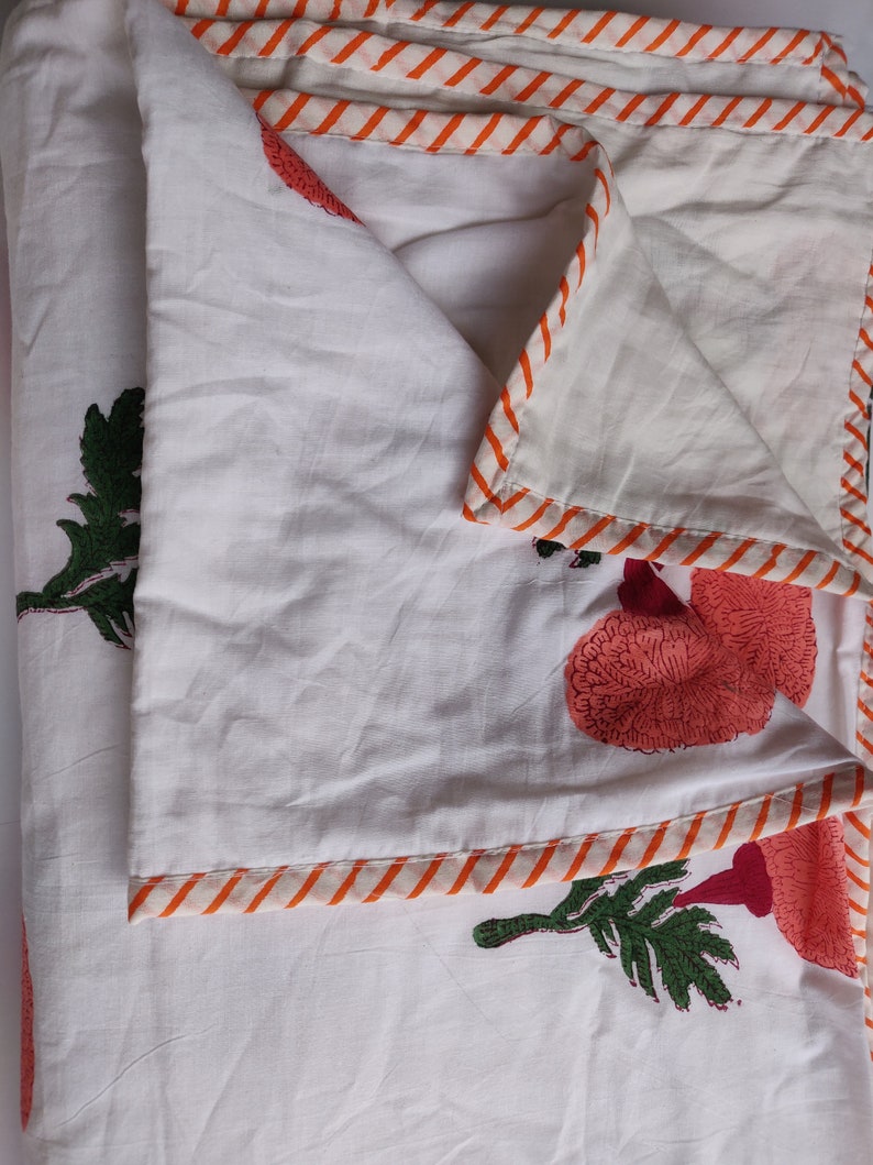 May include: White cotton quilt with a red and orange floral print. The quilt has a striped orange and white border.