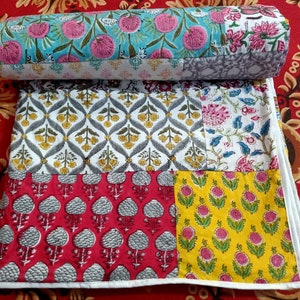 May include: A patchwork quilt featuring a range of floral designs in shades of pink, yellow, blue, and grey. The quilt is made from cotton fabric and has a white border.