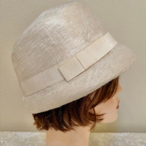 May include: A white fuzzy hat with a wide white satin ribbon. The hat is on a mannequin head.