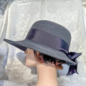May include: A dark gray sun hat with a wide brim and a dark ribbon band. The hat has a bow on the back and is made of a woven material. The hat is displayed on a mannequin head.