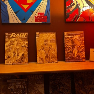 Könnte beinhalten: Ein Regal mit einer Auswahl an Comics, darunter The Flash, Batman und Thor. Die Comics sind alle in verschiedenen Farben und haben unterschiedliche Illustrationen. Das Regal ist aus Holz und hat eine hellbraune Oberfläche.
