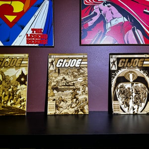 May include: Three framed comic book covers with the title "G.I. JOE" printed on each. The covers are made of wood and feature different scenes from the comic book.