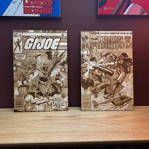 May include: Two wooden comic book covers featuring G.I. Joe and Transformers artwork. The G.I. Joe cover shows soldiers and a tank, while the Transformers cover depicts robots in action. The G.I. Joe comic is priced at $1.50.