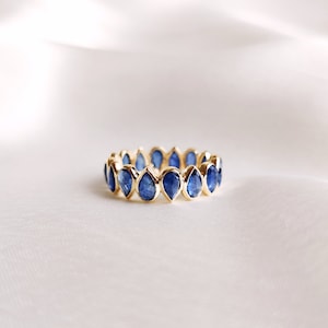 Puede incluir: Un anillo de banda de oro con una fila de zafiros azules en forma de lágrima.