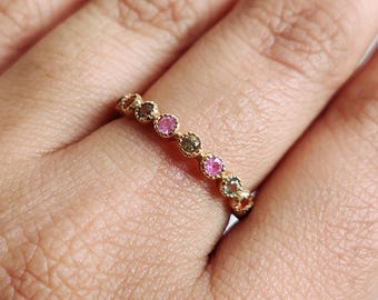 以下が含まれることがあります： カラフルな宝石が並んだゴールドのバンドリング。宝石はピンク、グリーン、ブラウンです。