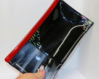 Könnte beinhalten: Eine schwarze Glasschüssel mit rotem Rand und schillernden Akzenten. Die Schüssel hat eine leicht geschwungene Form und ist perfekt zum Servieren von Snacks oder Vorspeisen.