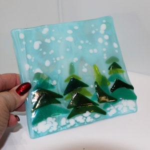 May include: A blue glass plate with a winter scene. The plate features a snowy background with white dots and green trees.