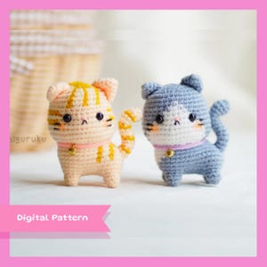 Könnte beinhalten: Zwei gehäkelte Amigurumi-Katzenspielzeuge. Eine ist hellorange mit gelben Streifen und die andere ist hellblau mit weißen Markierungen. Beide haben eine rosa Nase und schwarze Augen.  "Digitales Muster" steht auf einem rosa Banner unter den Spielzeugen.