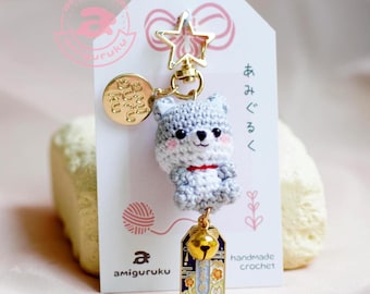 May include: A gray and white crocheted wolf amigurumi keychain with a gold star charm, a gold bell charm, and a gold tag with Japanese text. The keychain is hanging from a white card with the text "handmade crochet" and "amigurumi".