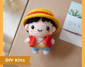 May include: A handmade crochet doll of a cartoon character wearing a yellow straw hat, red vest, and blue shorts. The doll has black hair and a small scar under its eye. The words "DIY Kits" are in a banner at the bottom.