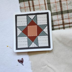Op de afbeelding: Een vierkante sticker met een quiltblokontwerp. Het ontwerp bevat een centraal perzikkleurig vierkant, een roodbruine ster en grijsgroene driehoeken op een crèmekleurige achtergrond, met zwarte stikseldetails en een zwarte rand. Rustiek ontwerp.