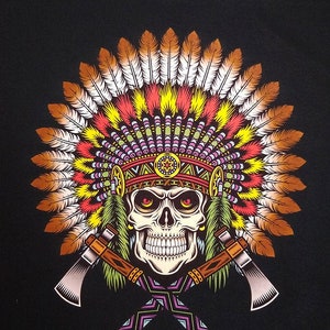 Może przedstawiać: Czarny t-shirt z nadrukiem graficznym przedstawiającym czaszkę w dużym, kolorowym pióropuszu. Czaszka ma czerwone oczy i znajduje się nad dwoma skrzyżowanymi tomahawkami ze wzorzystymi rękojeściami, utrzymanymi w żywych odcieniach żółci, czerwieni i brązu.