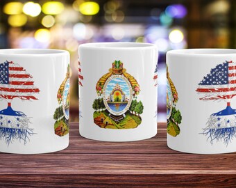 Op de afbeelding: Drie witte keramische mokken met een ontwerp met een boom met de Amerikaanse vlag als bladeren en de Hondurese vlag als wortels. De middelste mok heeft het Hondurese wapenschild in het midden.