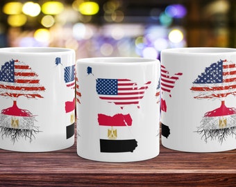 Op de afbeelding: Drie witte keramische mokken met een boomontwerp. De boom is gemaakt van de Amerikaanse vlag en de wortels zijn de Egyptische vlag. De mokken staan op een houten oppervlak.