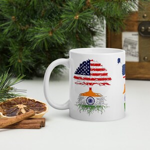 Op de afbeelding: Witte keramische mok met een boomontwerp met de Amerikaanse vlag als bladeren van de boom en de Indiase vlag als wortels. De mok heeft een zwart handvat.