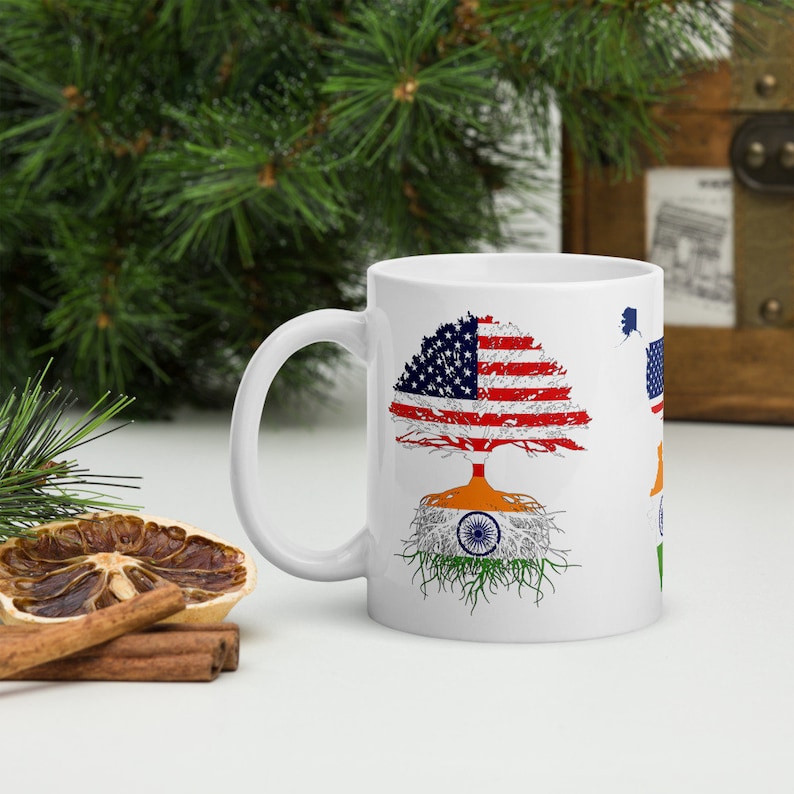 Op de afbeelding: Witte keramische mok met een boomontwerp met de Amerikaanse vlag als bladeren van de boom en de Indiase vlag als wortels. De mok heeft een zwart handvat.