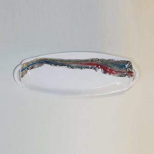 May include: White oval serving dish with a colorful abstract design. The design features a mix of blue, red, and silver metallic accents. The dish has two small handles on either side.