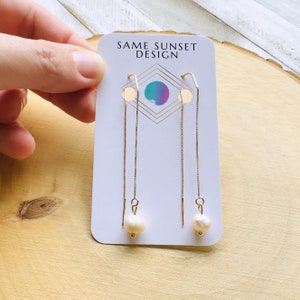 May include: Gold-tone threader earrings with a freshwater pearl drop. The earrings are displayed on a white card with the text "SAME SUNSET DESIGN" and a geometric design with a watercolor effect.