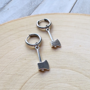 May include: A pair of silver hoop earrings with a small silver axe charm hanging from each hoop.