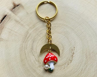 May include: Gold keyring with a crescent moon charm and a red and white mushroom charm with white spots. The mushroom has a green stem and a white pearl.
