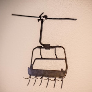 May include: A metal wall-mounted sculpture of a ski lift gondola with hooks for hanging items.