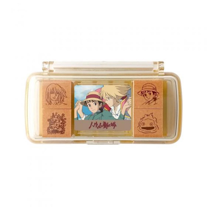 May include: A clear plastic case with six wooden stamps featuring characters and images from the animated film "Howl's Moving Castle". The stamps include Howl, Sophie, Calcifer, and the moving castle. The case has a sliding lid and the text "Howl no Ugoku Shiro" is printed on the front.