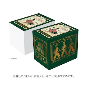 May include: A 2021 daily calendar set in a dark green box with gold foil illustrations of mail carriers and the text Daily Calendar 2021. The top of the box features a stamp-like graphic of a character walking on a globe with the text 2021.