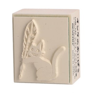 May include: A beige rubber stamp with a raised image of a cat holding a feather quill. The stamp is labeled "Ink of the Cat" and "TSW-149 Ghibli/Jiji and Fountain Pen".
